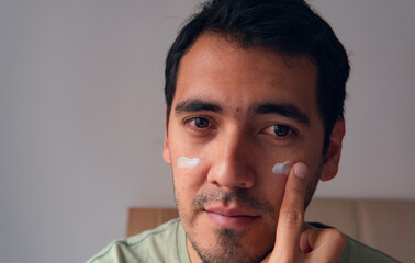 portrait of latin man applying moisturizer on his face