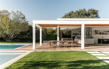 A white wood pavilion with an outdoor dining area and wooden deck, surrounded by green grass near the pool in front of a modern minimalist house.