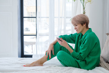 a woman in a green suit and with a phone in her hands sits on a large bed
