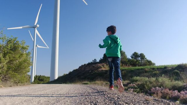 A joyful 6-year-old boy runs freely through a field, surrounded by towering windmill turbines, symbolizing hope for a sustainable, green energy future amidst the challenges of climate change