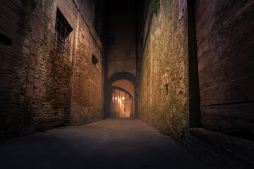 Dark narrow empty medieval street in historical center of European town, Siena, Italy