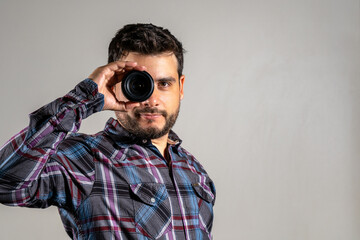 Hombre apuesto mirando a través de un lente de fotografía digital. Fotografia con copy space y fondo blanco - obrazy, fototapety, plakaty