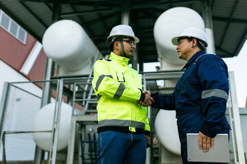 Two men in safety gear shake hands. One of them is holding a tablet. Scene is professional and friendly