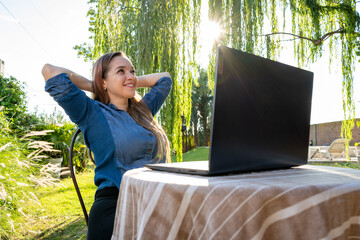 Mujer trabajando feliz con su laptop al aire libre, en el jardín de su casa