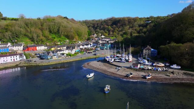 Aerial shot travelling over water towards a small fishing village and  harbour with boats at Fishguard, Pembrokeshire, Wales.