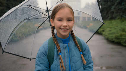 Little European girl looking at camera smiling holding umbrella rain weather park walk outside daughter child learner kid pupil toothy dental smile joy fun positive female wet seasonal droplet climate - Powered by Adobe