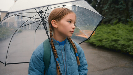 Tired little girl schoolgirl child looking at camera bored unhappy bad weather rain umbrella city park outdoors fatigue damp wet face daughter kid pupil offspring lonely sadness rainfall discomfort