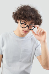 Smiling and handsome, the young man wears glasses. He looks into the camera with his blue eyes, man portrait with eyeglasses isolated against a gray background