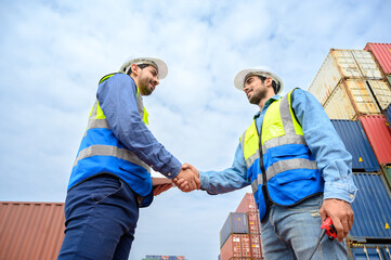 Two engineer container cargo wearing white hardhat and safety vests in successful handshake together at container yard. success in logistics business import export industry
