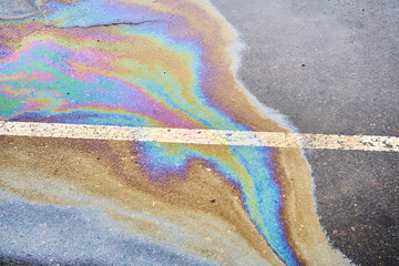 Oil spillage on wet pavement, parking lot with dividing lines, underscoring the environmental...