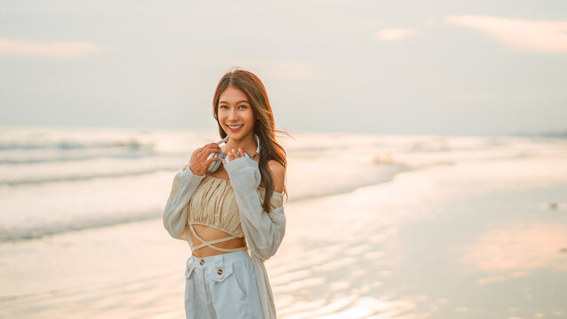 Relax asian woman wearing headphones listening to music breathing fresh air enjoying beautiful sunset over the sea beach, copy space.