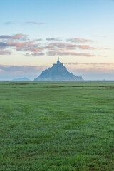 Silhouette of Mont Saint Michel cathedral on the island with green meadow at sunrise, Normandy, France. Tidal island with medieval gothic cathedral in Normandie. Vertical orientation - 790900476