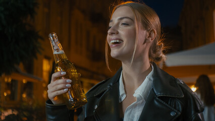 European young woman drinking alcohol holding bottle of beer enjoying satisfied girl smiling city...