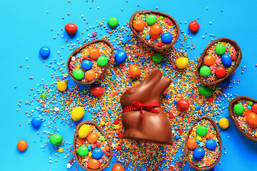 Chocolate bunny and candy, colored sugar sprinkles on a blue background, top view. Easter...