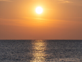 The sun sets over a calm ocean, with golden light reflected on the water