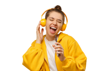 Trendy young woman singing favorite song out loud in phone as mic, wearing yellow wireless headphones. Karaoke online app