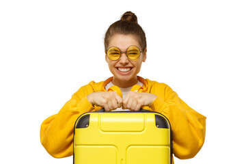 Young funny smiling woman in yellow hoodie and colored glasses holding handle of travel suitcase,...