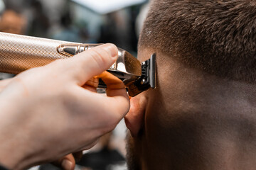 Coiffeur shaves client hair with electrical trimmer in modern barbershop closeup. Barber does...