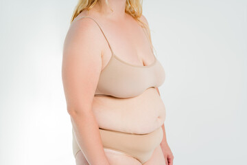 Fat woman in beige underwear on gray background, overweight female body, plastic surgery concept
