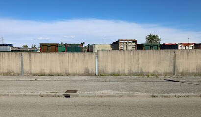 Surrounding wall made of concrete blocks with truck trailers of a transportation company in a row behind. Road in front, sky above. Background for copy space.