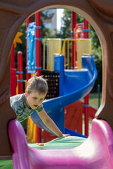 Portrait of a boy playing outside. Arched framing, colorful playground in the background