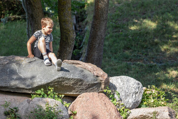 Naklejka na ściany i meble Portrait of a small boy sitting on top of large rocks