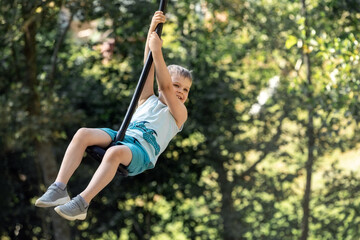 Cheerful little boy swings on a rope swing against a dreamy background of summer foliage. the photo...