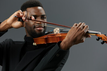 Talented African American man in black suit playing the violin on a sleek gray background