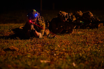 Naklejka premium Soldiers in camouflage uniforms aiming with their rifles.ready to fire during Military Operation at night, soldiers training in a military operation