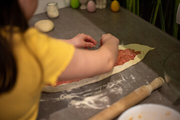 Obraz na płótnie Canvas A child prepares pide, Turkish pizza. A girl rolls out dough to make a meat pie.