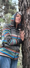 Adult woman leaning against a tree trunk, with a sweatshirt covering her head and with one hand...