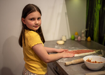 A child prepares pide, Turkish pizza. A girl rolls out dough to make a meat pie.