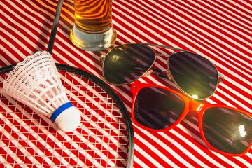 Pair of sunglasses and a racket are on a striped table