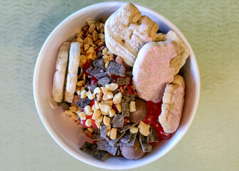 A cup of frozen yogurt covered with toppings including nuts, chocolate chips, boba, and animal cookies