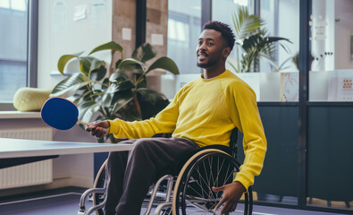 Portrait of joyful impaired young man in wheelchair playing a table tennis in the office