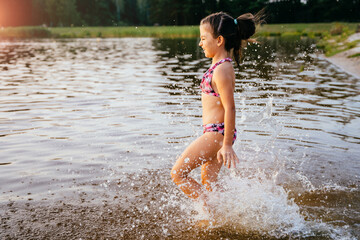 Happy children run from the shore into the water. Summer children's vacation on shore of a lake or river.