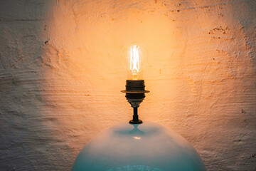 Glowing Edison Bulb Over Glass Lampshade Against Textured Wall