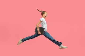 Girl in mid-jump holding a laptop on pink background