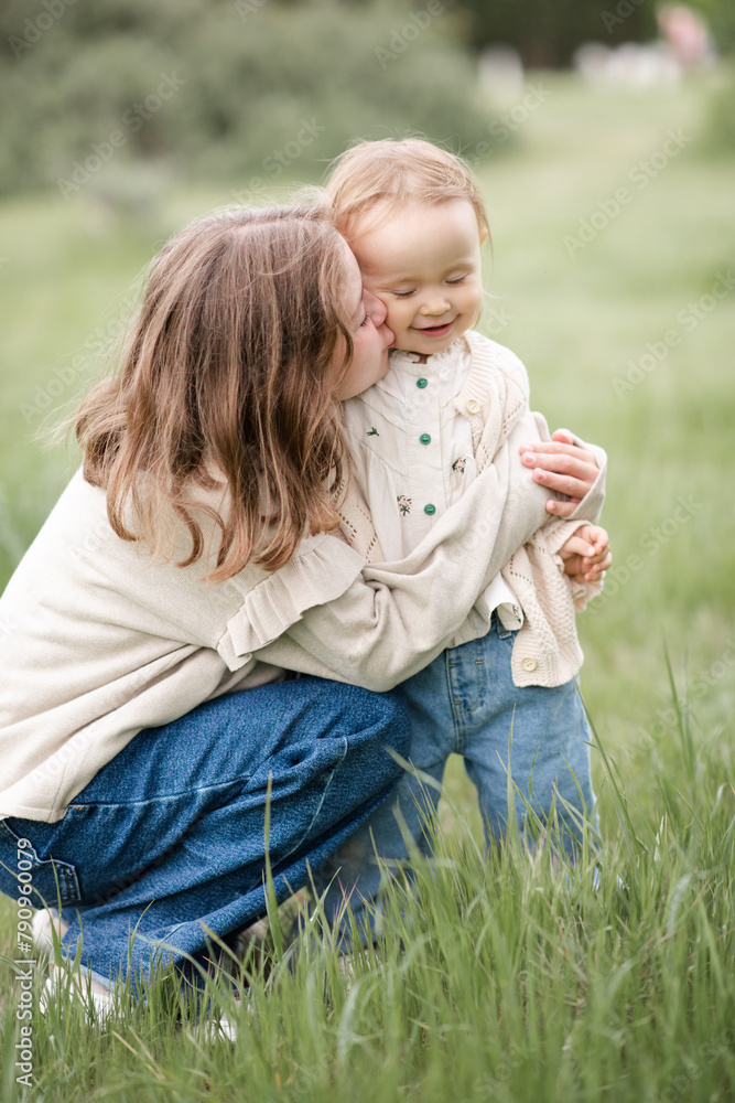 Wall mural child girl kissing baby wearing stylish clothes over green grass lawn outdoor. summer season. childh