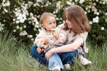 Cute baby and kid girl with flowers together outdoor. Looking at each other. Childhood.