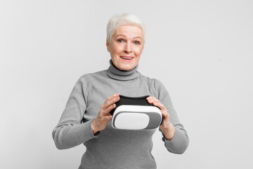 Elderly woman with VR headset amazed on grey background