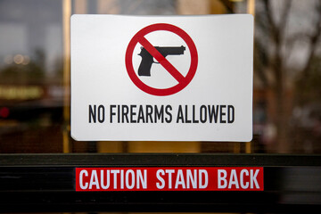 Sign stating No Firearms allowed with red circle and red line and a sign stating Caution Stand Back