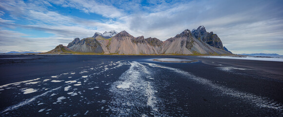 landscape in panorama format of the famous mountain range Vestrahorn with a beach of wet black...