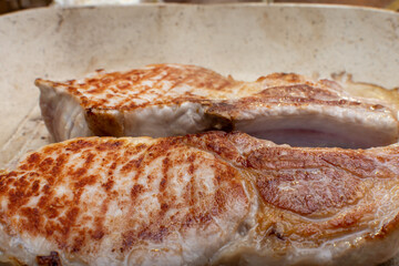 Two meat pieces sizzle in a pan, preparing a delicious dish