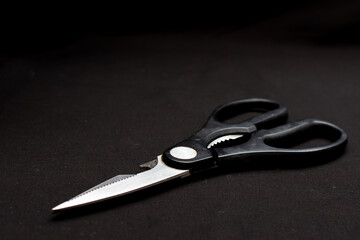 A pair of scissors with sleek black handles on a black surface