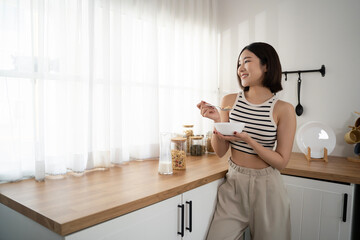 Asian woman in cozy and comfortable clothes sitting on kitchen counter while picking up some beans. Healthy living home and domestic life. Rich nutrition lifestyle - 790971460