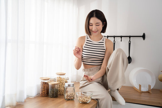 Asian woman in cozy and comfortable clothes sitting on kitchen counter while picking up some beans. Healthy living home and domestic life. Rich nutrition lifestyle