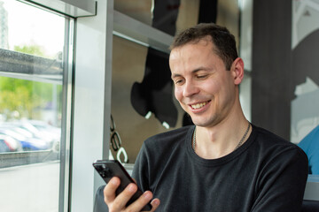A man in a black sweater smiles while using his mobile phone