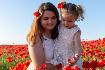 A woman and a girl stand among red flowers in a field, smiling happily