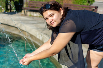 Woman smiling while washing hands in fountain near grassy area on a sunny day